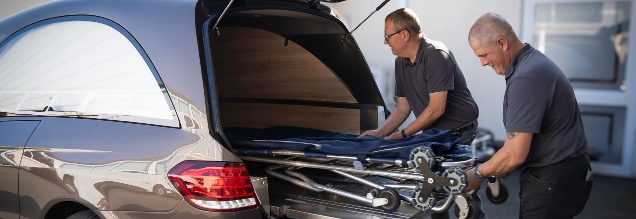 Ausladung der Trage aus dem Bestattungswagen Ausladung der Trage aus dem Bestattungswagen